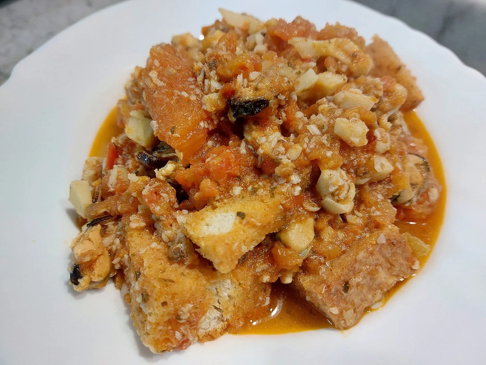 Piatto di cacciucco con pezzi di pesce, cozze e pane abbrustolito immersi nel sugo di pomodoro
