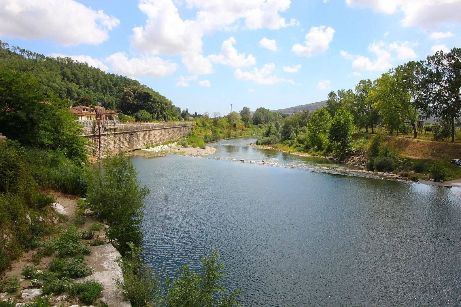 Il fiume Serchio a Ripafratta tra argini alberati e colline boscose sotto un cielo con nuvole bianche